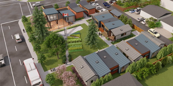 An aerial view of a small community of modern tiny homes arranged around a central green space with trees, garden beds, and walking paths, bordered by urban streets with buses and cars.
