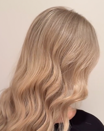 Close-up of soft, wavy blonde hair with a lived-in colour look, showcasing a seamless blend and smooth finish.