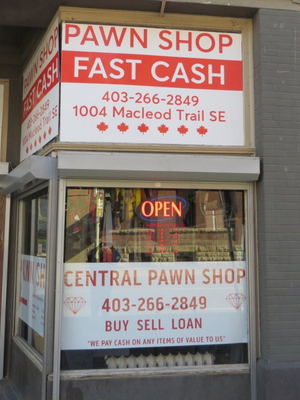 An image of the front of Central Pawn Shop storefront, with an Open sign, and red text over white background on signs. Text that says "FAST CASH"