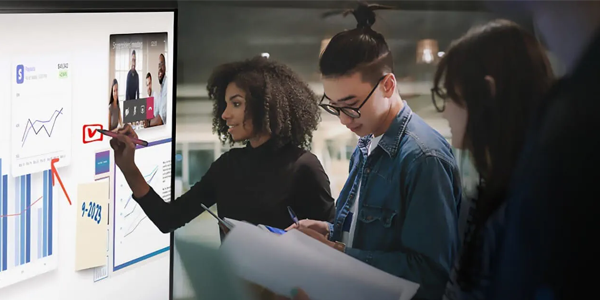 A group of young professionals collaborating around an interactive digital whiteboard displaying charts, sticky notes, and a video call, showcasing SMART Technologies’ tools for real-time teamwork and engagement.