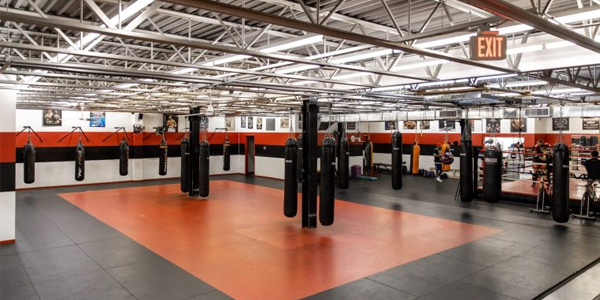 Interior of Team Impact's spacious boxing gym featuring hanging heavy bags, padded flooring, and a full-size boxing ring, designed for training youth and adults in a safe and supportive environment.